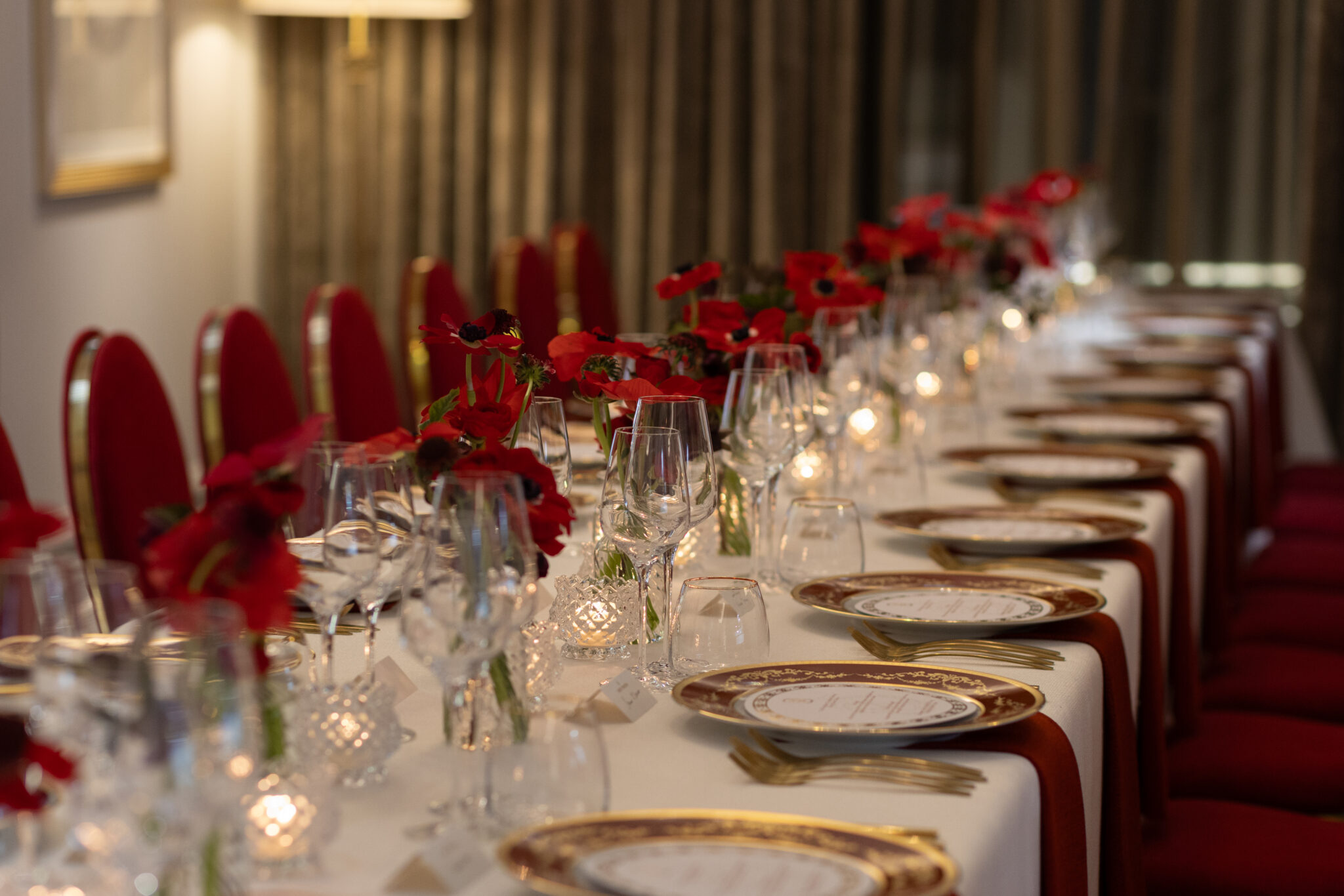 Long table white linen with red velvet chairs flower vases