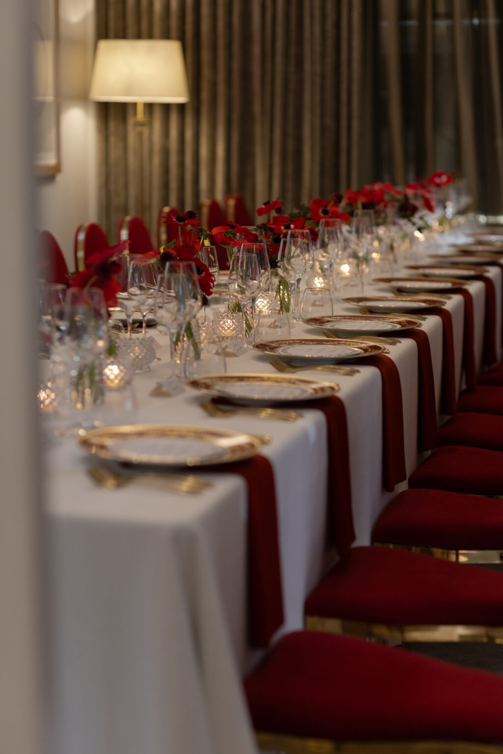 Row of red velvet chairs at white table with place settings