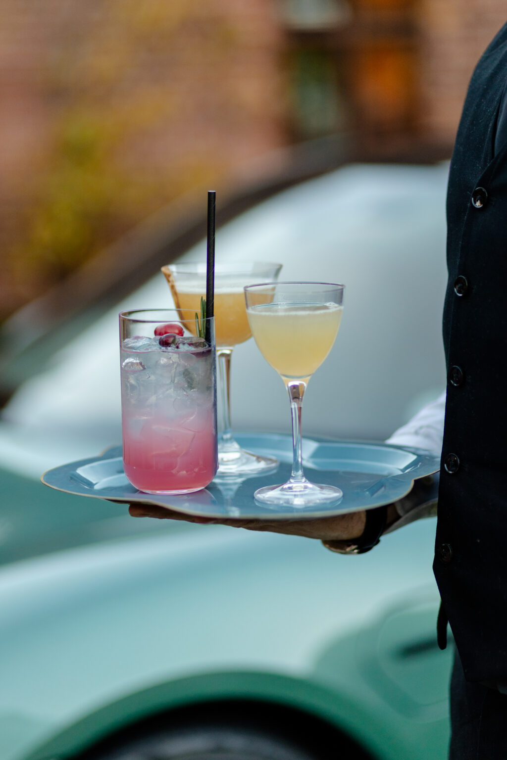 cocktails on tray held by waiter car in background